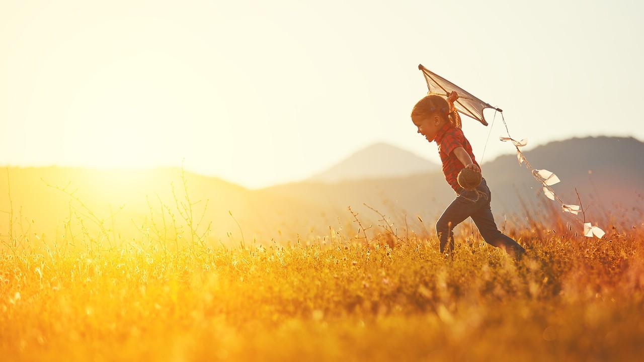 Child running through wheat field with kite