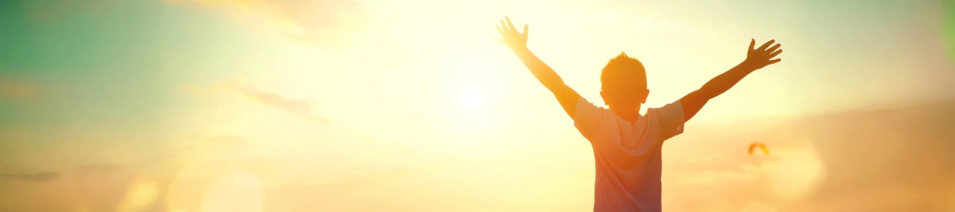 Boy silhouetted with his arms raised in the sunshine