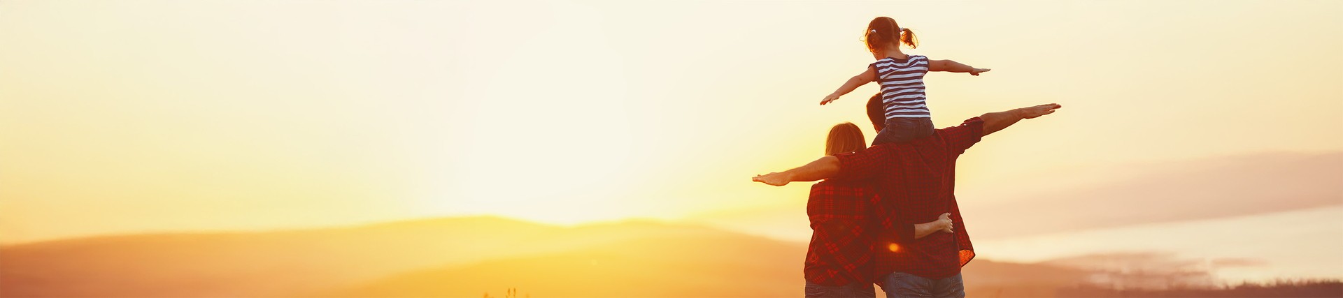 Two parents with their child in a cornfield, arms outstretched in the sunshine.