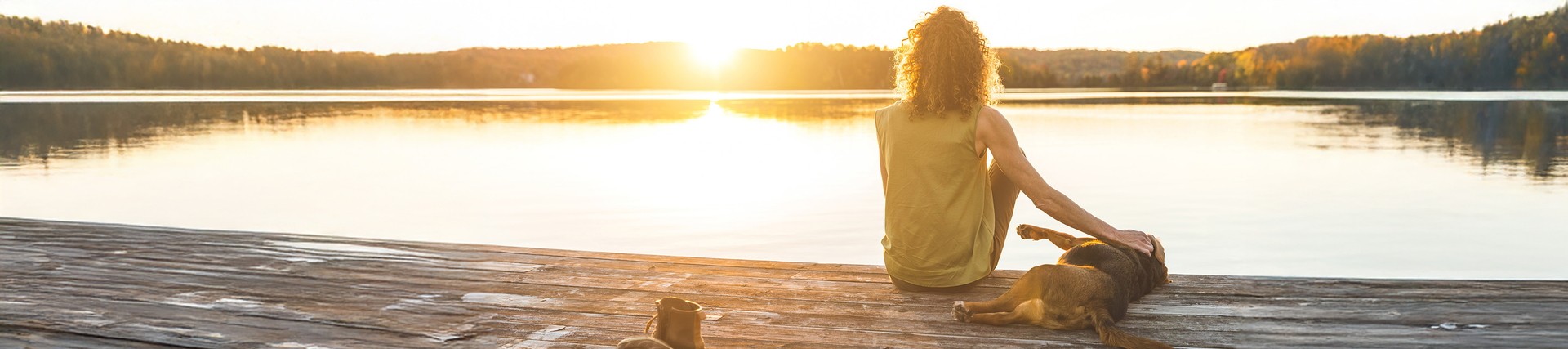 Woman sat on jetty next to lake, with sleeping dog